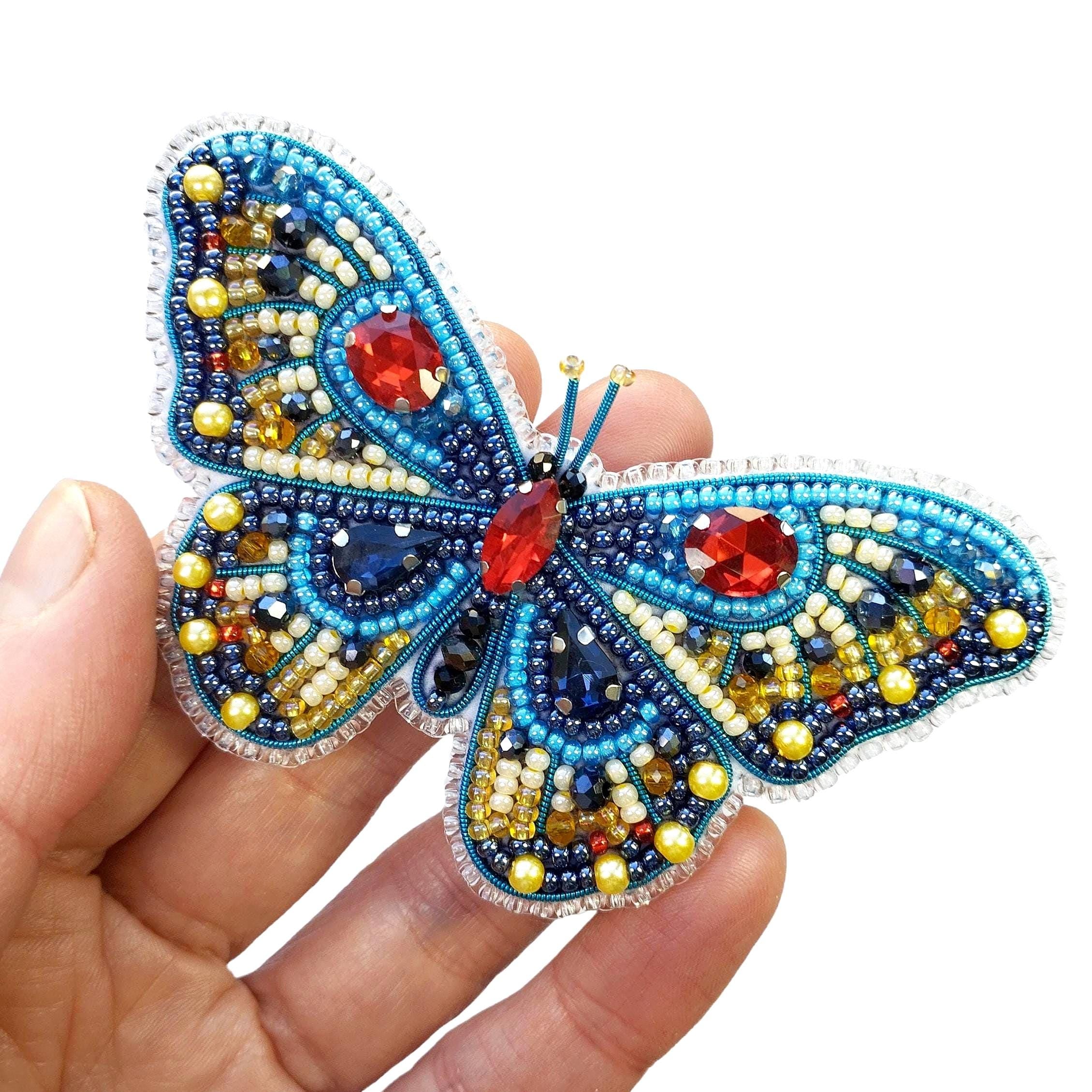 a hand holding a beaded butterfly brooch